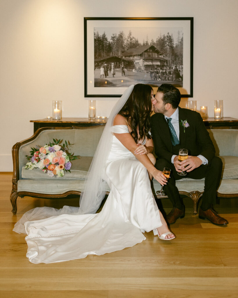 bride and groom kiss on a couch inside of the Stanley Park Pavilion